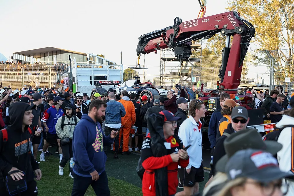 Fans dringen het circuit binnen terwijl marshalls de auto van Nyck de Vries, AlphaTauri AT04, op een vrachtwagen laden.