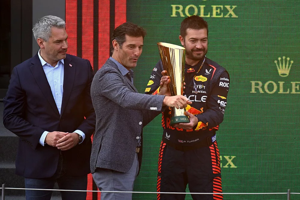 Un repr&eacute;sentant Red Bull re&ccedil;oit le troph&eacute;e sur le podium des mains de Mark Webber