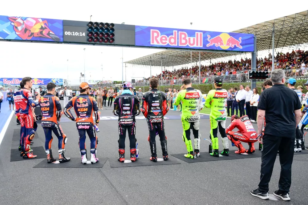 The riders stand for the national anthem on the grid