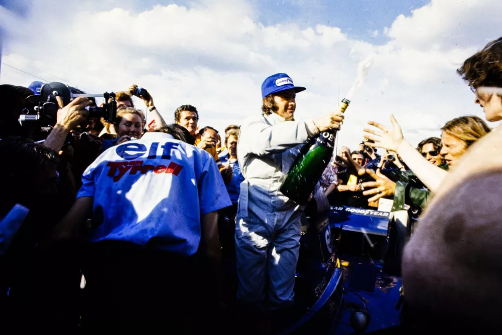 Race winner Jackie Stewart celebrates with a bottle of champagne in parc ferme.