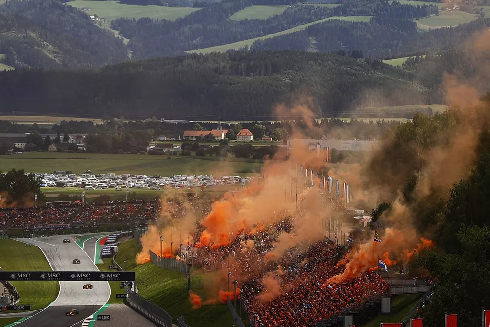 Lando Norris, McLaren MCL36, Daniel Ricciardo, McLaren MCL36, Lance Stroll, Aston Martin AMR22, as orange smoke erupts from the grandstands