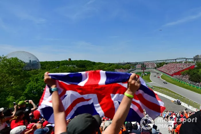 Un fan ondea la bandera de Reino Unido mientras Lewis Hamilton, Mercedes AMG F1 W10, lidera por delante de Charles Leclerc, Ferrari SF90, Daniel Ricciardo, Renault R.S.19, y el resto de la parrilla