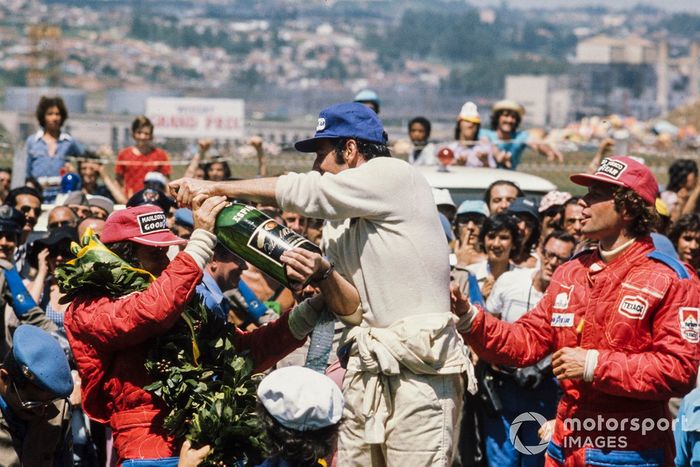 Carlos Pace celebra a vitória no pódio, servindo champanhe ao colega brasileiro Emerson Fittipaldi, 2º classificado, com Jochen Mass à direita, 3º classificado