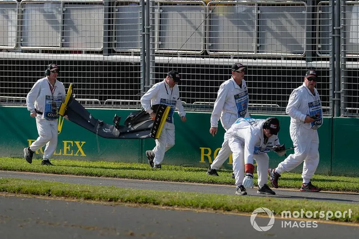 Oficiales remueven el alerón delantero y los escombros pertenecientes al coche de Daniel Ricciardo, Renault, del circuito