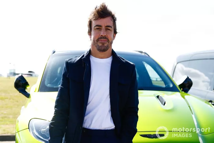 Fernando Alonso, Aston Martin F1 Team, sostiene su casco mientras se apoya en la parte delantera de un Aston Martin DBX.