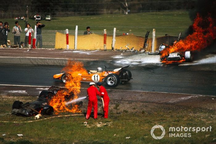 Bruce McLaren, McLaren M14A Ford, conduce entre el ardiente BRM P153 de Jackie Oliver y el Ferrari 312B de Jacky Ickx mientras los oficiales trabajan para extinguir las llamas.